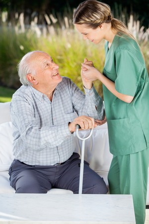Female Caretaker Helping Elderly Man To Get Up From Couchの写真素材