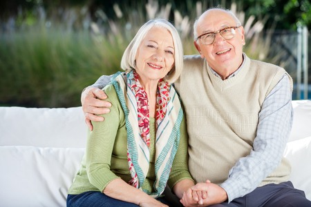 Happy Senior Man Sitting With Arm Around Woman On Couchの写真素材