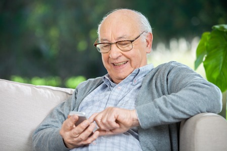 Smiling Senior Man Text Messaging Through Mobilephoneの写真素材