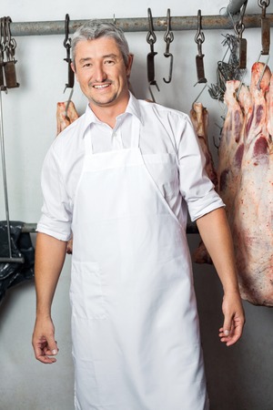 Butcher Standing Against Meat Hanging In Butcheryの写真素材