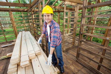 Smiling Carpenter Measuring Wooden Plank At Construction Siteの写真素材