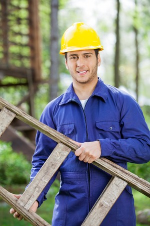 Smiling Worker Carrying Ladder At Construction Siteの写真素材