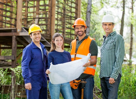 Happy Architects With Blueprint At Construction Site
