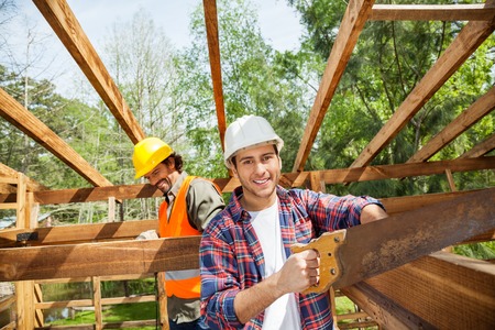 Happy Worker Cutting Wood With Handsaw At Construction Siteの写真素材