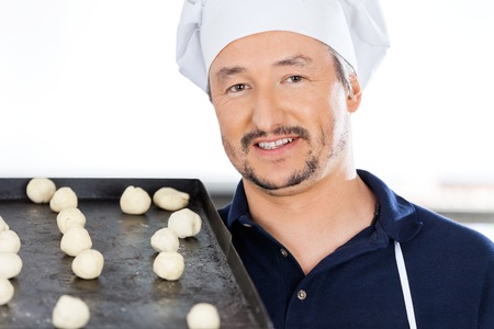 Confident Chef Carrying Baking Sheet With Dough Balls At Kitchenの写真素材