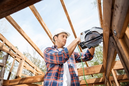 Construction Worker Using Electric Saw On Timber Frame At Siteの写真素材