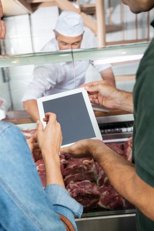 Cropped image of mature couple using digital tablet at butchery counterの写真素材