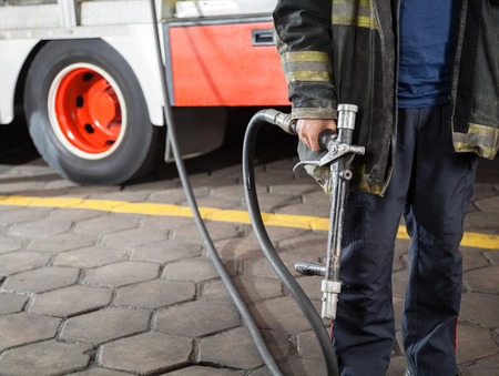 Midsection of firefighter holding water hose while standing at fire stationの写真素材