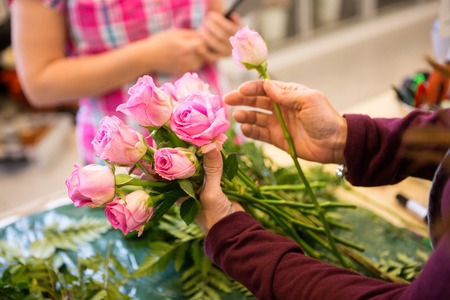 Cropped image of female worker making bouquet of roses for customer in flower shop