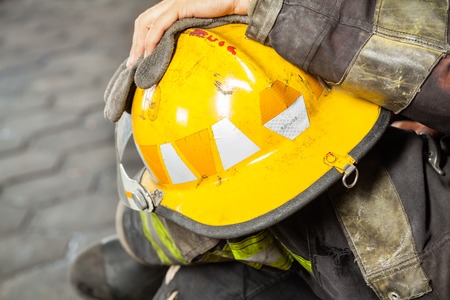 Cropped image of male firefighter holding yellow helmet at fire station