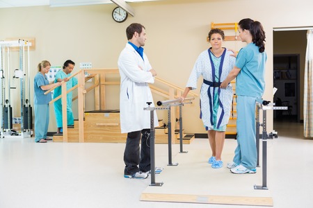 Physical therapists assisting female patient in walking with the support of handrailsの写真素材
