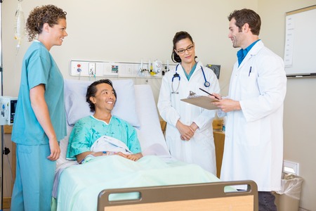 Young doctors discussing notes while happy patient and nurse looking at them in hospital roomの写真素材