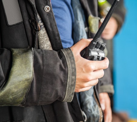 Midsection of firefighter holding walkie talkie at fire station