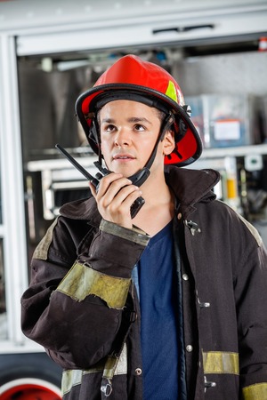 Confident young firefighter looking away while using walkie talkie at fire stationの写真素材