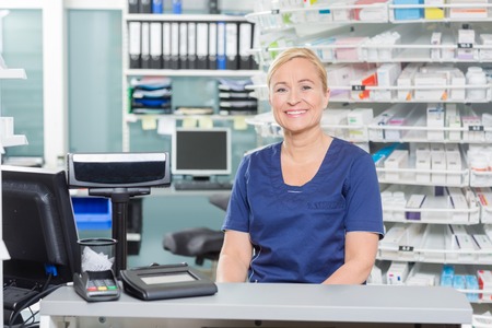 Portrait of confident assistant sitting at cash counter in pharmacyの写真素材
