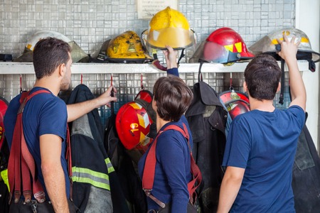 Male and female firefighters removing helmets from shelf in fire stationの写真素材