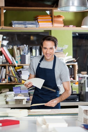 Portrait of smiling mid adult male worker holding papers and ruler at table in paper industry