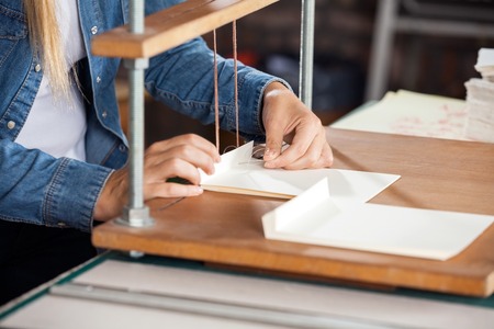 Midsection of female worker binding papers at workbench in factoryの写真素材