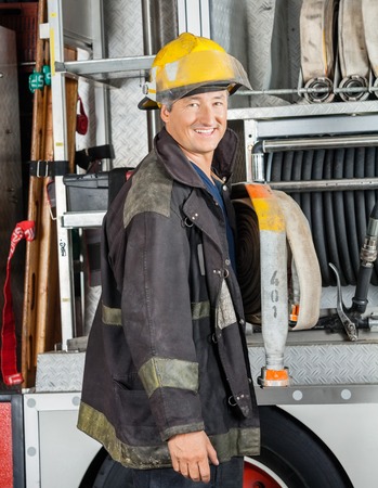 Side view portrait of happy male firefighter standing by truck at fire stationの写真素材