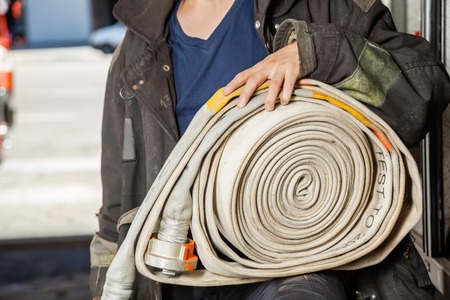 Midsection of young fireman holding water hose at fire stationの写真素材