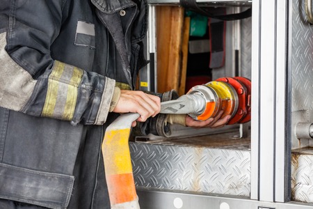 Midsection of male firefighter adjusting hose in truck at fire stationの写真素材