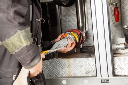 Midsection of mature fireman adjusting water hose in truck at fire stationの写真素材