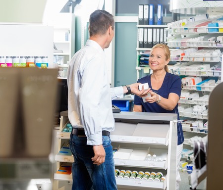 Smiling female pharmacist giving product to male customer in pharmacyの写真素材