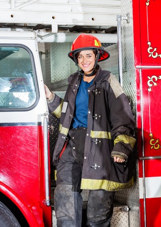Portrait of happy female firefighter in uniform standing on truck at fire stationの写真素材