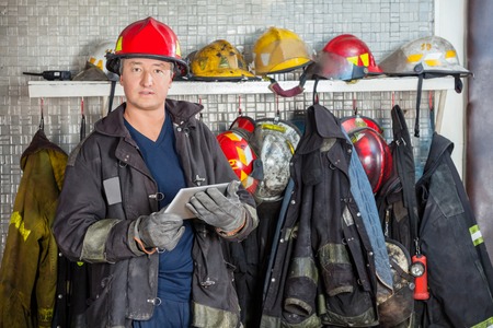 Portrait of mature fireman in uniform holding digital tablet at fire station