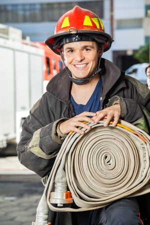 Portrait of happy young fireman holding water hose at fire station