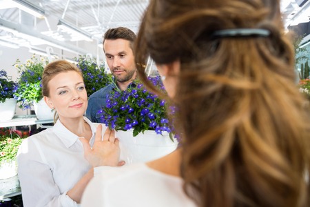 Happy couple being assisted by florist in buying flower plant at shopの写真素材