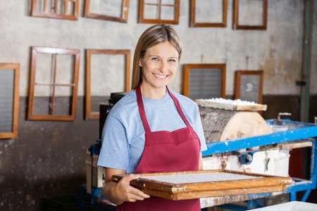 Portrait of confident mid adult female worker holding mold at paper factoryの写真素材