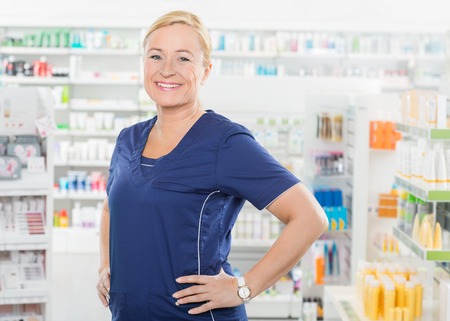 Portrait of confident female pharmacist standing with hands on hip in pharmacyの写真素材