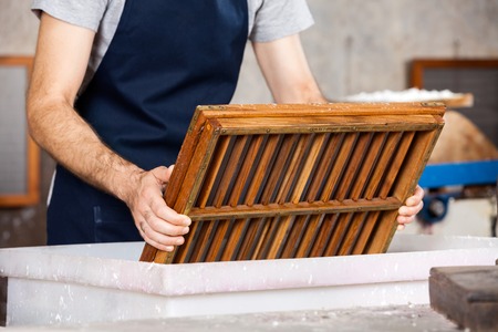 Midsection of male worker dipping mold in pulp and water at paper factoryの写真素材
