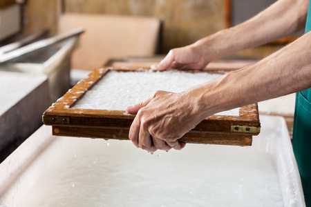 Cropped image of male worker dipping mold in pulp and water at paper factoryの写真素材