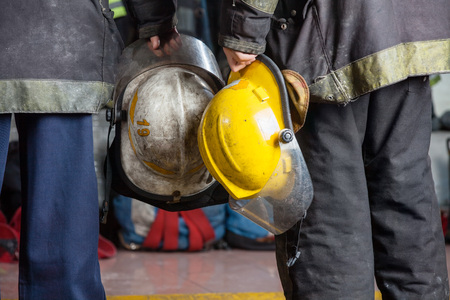 Midsection rear view of firemen holding helmets at fire stationの写真素材
