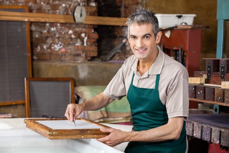 Portrait of confident mature male worker cleaning paper with tweezers in factory