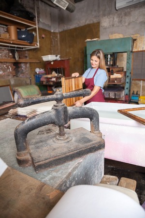 Closeup of paper press machine with worker working in background at factoryの写真素材