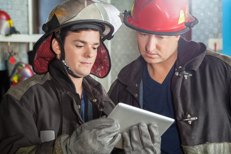 Young and mature firemen using tablet computer at fire stationの写真素材