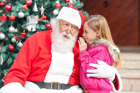 Girl telling wish in Santa Claus's ear against Christmas treeの写真素材
