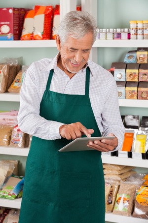 Happy senior male owner using digital tablet in supermarketの写真素材