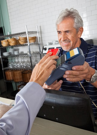 Senior salesman holding electronic reader while customer paying through smartphoneの写真素材