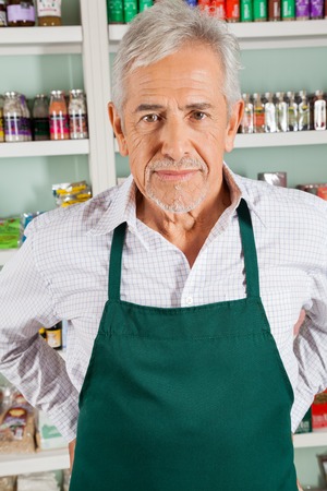 Portrait of confident senior male owner standing in grocery storeの写真素材