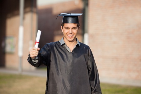 Portrait of confident male student showing diploma on graduation day at university campusの写真素材