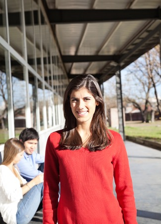 Portrait of happy young woman smiling with students in background on college campusの写真素材