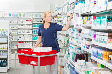 Mature female chemist arranging products in pharmacyの写真素材