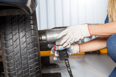 Cropped of female mechanic using pneumatic wrench to fix car tire at repair shopの写真素材