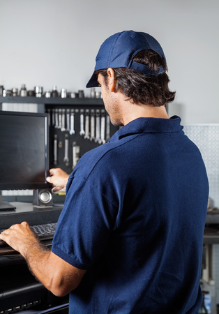 Rear view of male mechanic using computer in garage