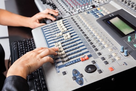 Cropped image of male and female professional's hands working on audio mixer in recording studio