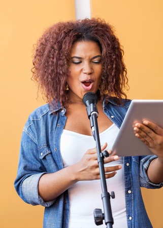 Young female singer holding tablet computer while performing in recording studioの写真素材